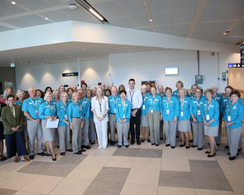 Group photo of Gold Coast Airport ambassadors wearing blue jackets and name tags in terminal setting.