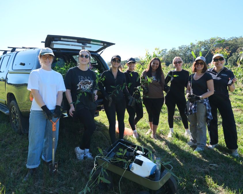 Group of Queensland Airports Limited employees outdoors with gardening tools and plants during environmental activity.