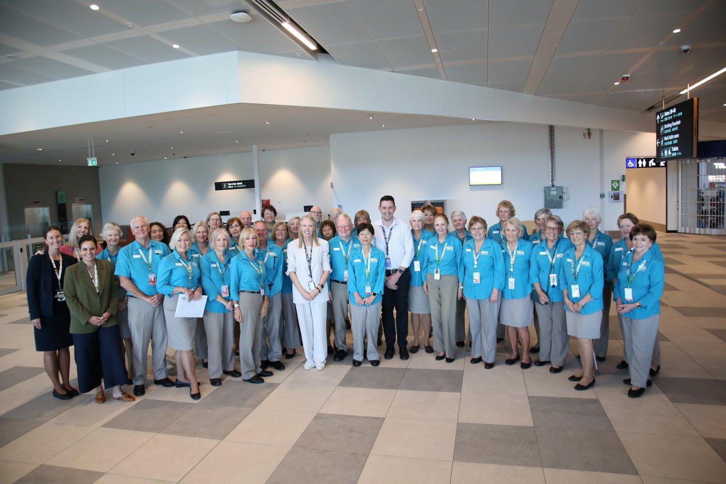Group photo of Gold Coast Airport ambassadors wearing blue jackets and name tags in terminal setting.
