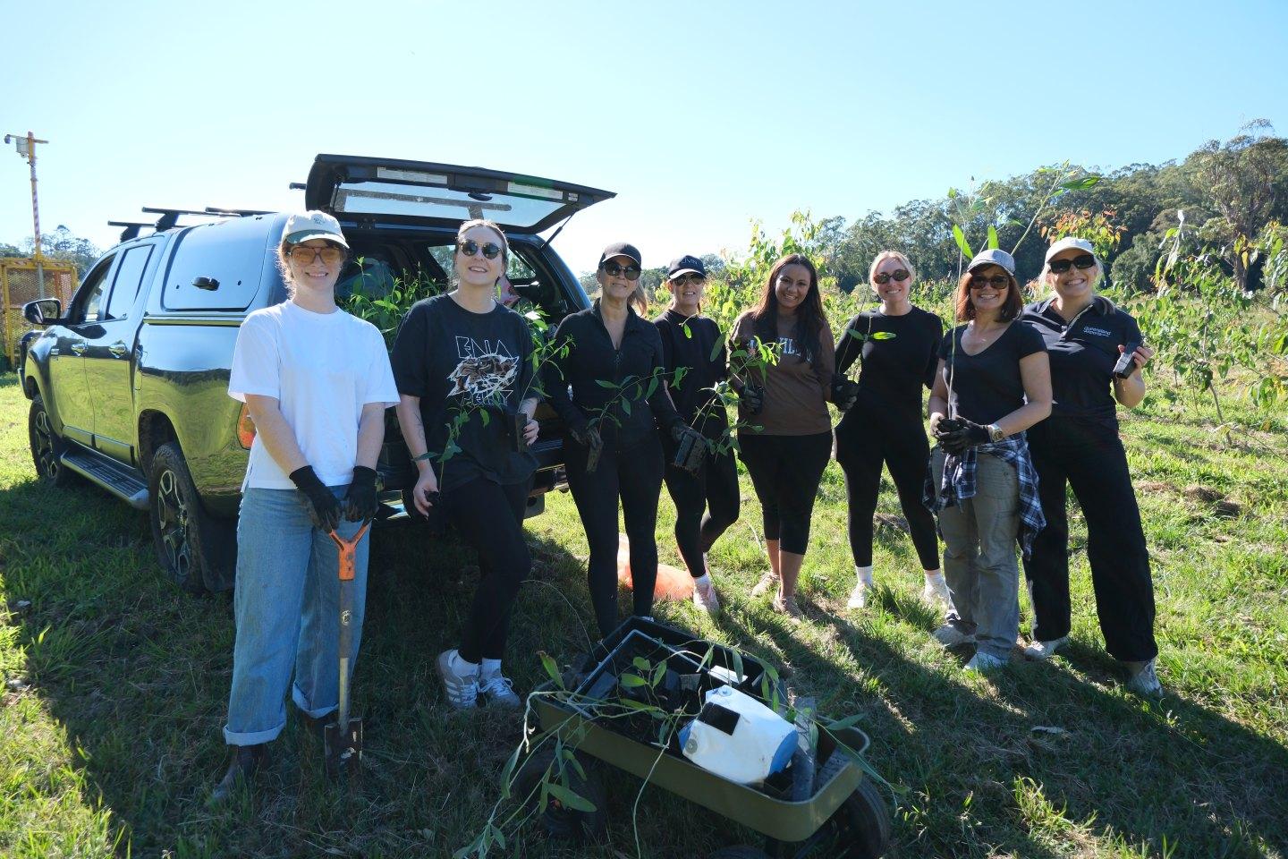 Group of Queensland Airports Limited employees outdoors with gardening tools and plants during environmental activity.