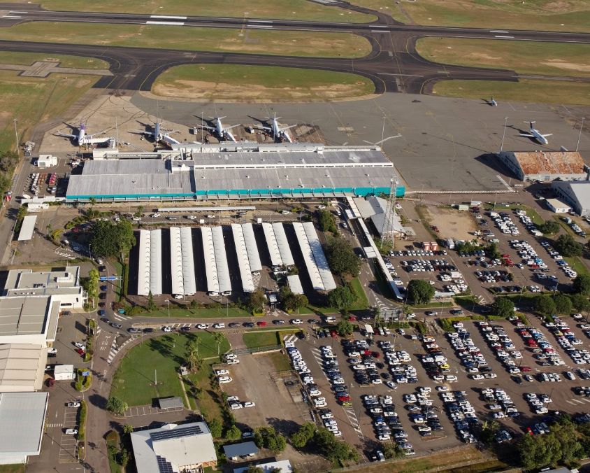 Aerial view of Townsville Airport showing terminal, parked aircraft, parking lots, and surrounding infrastructure.