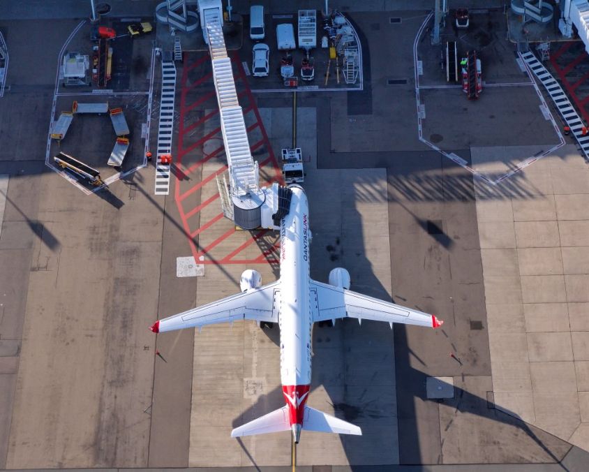 Aircraft docked at airport gate with jet bridge and ground service vehicles, showcasing operational facilities available to airline partners at QAL.