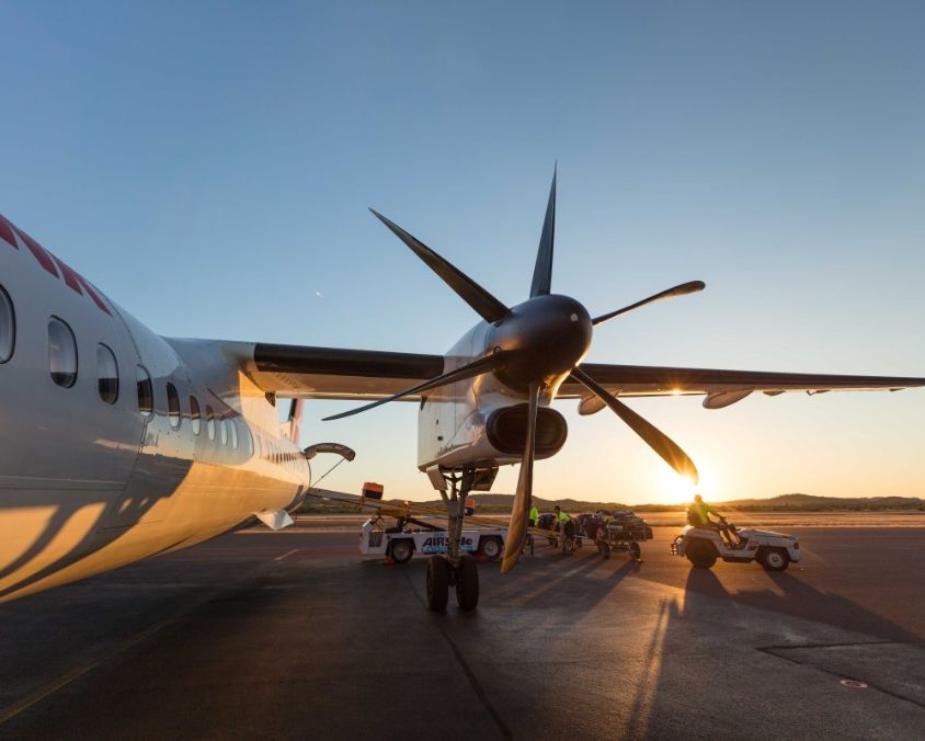 Propeller aircraft on the tarmac at sunrise with ground crew preparing for operations.