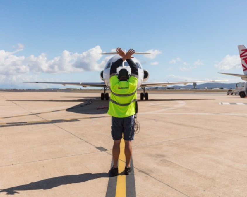 Townsville airport ground crew member signaling aircraft to stop with crossed arms, demonstrating standard safety protocol.